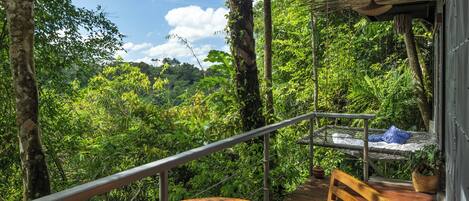 A wooden deck with a round table and a bench, overlooking a lush forest.