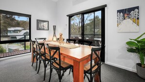A modern dining room with a wooden table and black chairs, large windows, and a painting on the wall. - Snowbound 2 - Family Ski Chalet, 5 minute walk to the slopes (Thredbo)
