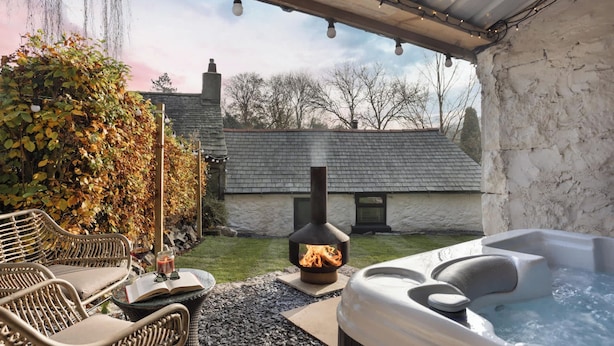 A patio area with a hot tub, a fire pit, outdoor seating, and a stone wall. - Mead Cottage | Ridgestone (Lindale)