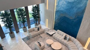 A spacious lobby with a large curved sofa, two round coffee tables, and potted plants. - Stylish Marina-Front 2BR | Dubai Marina | Near Top Attractions (Dubai)