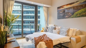 A modern hotel room with a large bed, a sofa, a view of a building through floor-to-ceiling windows, and a painting on the wall. - Stylish Marina-Front 2BR | Dubai Marina | Near Top Attractions (Dubai)