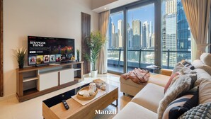 A modern living room with a large TV displaying 'Stranger Things', a sofa, a coffee table with a tray, and a city view through large windows. - Stylish Marina-Front 2BR | Dubai Marina | Near Top Attractions (Dubai)
