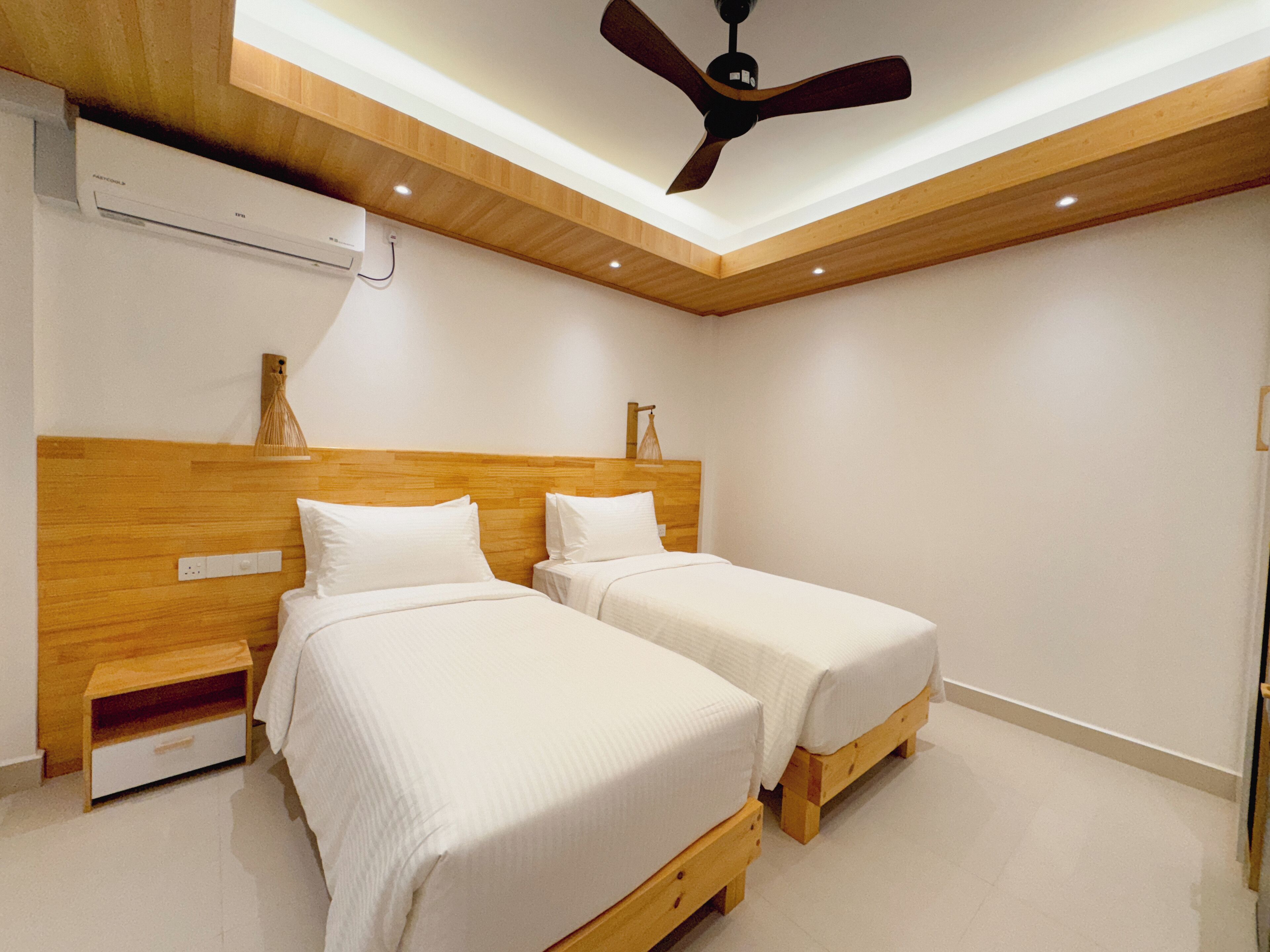 A modern bedroom with two beds, wooden headboards, a ceiling fan, and recessed lighting.