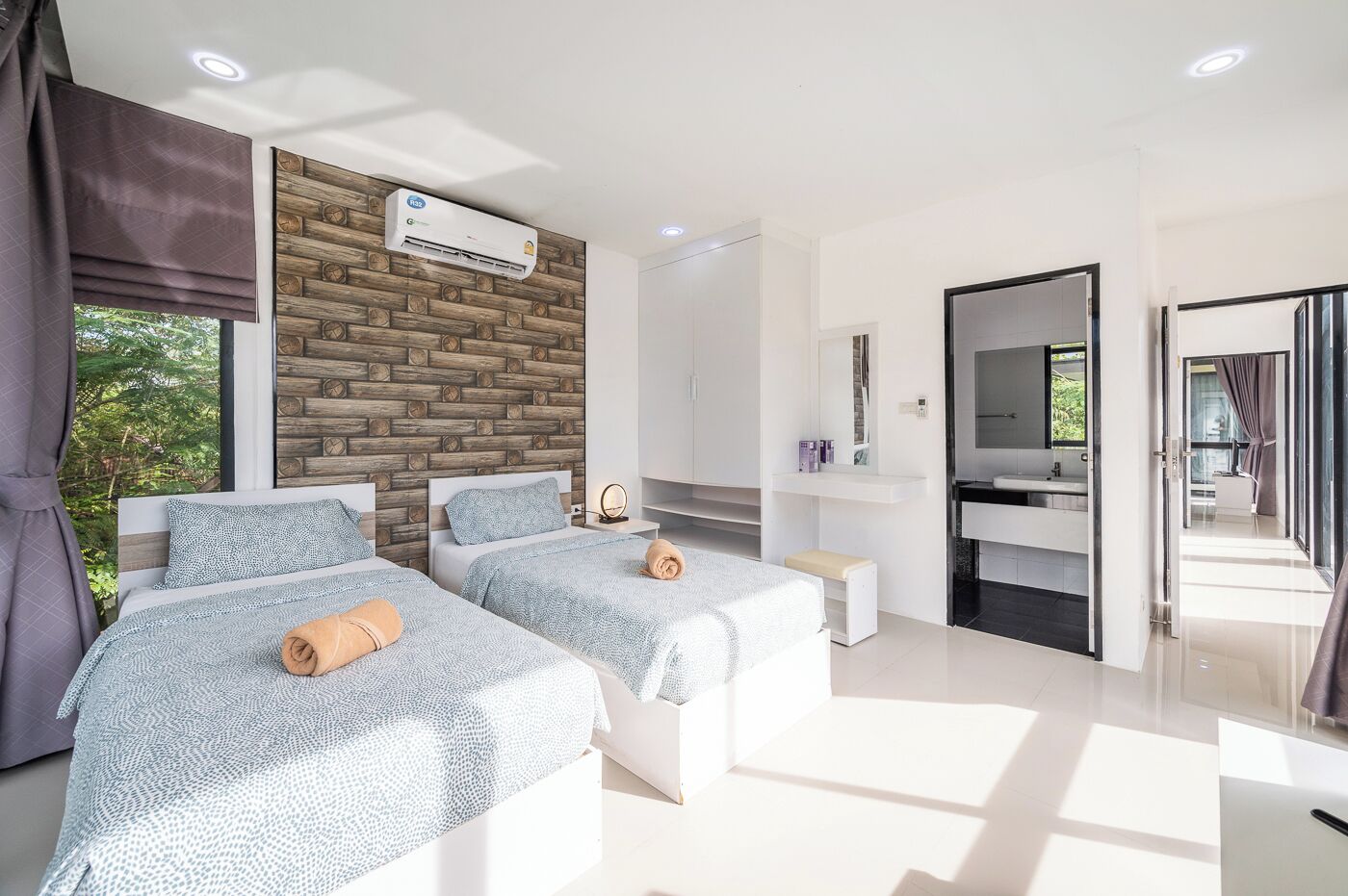 Une chambre d’hôtel moderne avec deux lits, un mur d’accent en bois, un grand miroir et une salle de bain dotée d’un comptoir noir.