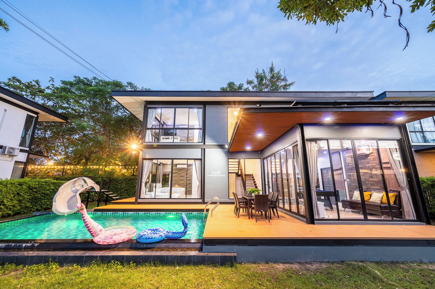 A modern two-story house with a swimming pool, outdoor seating area, and a slide.