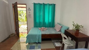 A small, well-lit room with a bed, a table, and a chair. There is a window with curtains, a door leading outside, and a tiled floor. - moonlight inn catangnan  (General Luna)