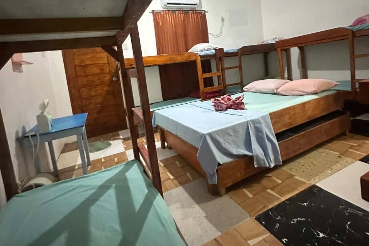 A dormitory room with two bunk beds, a desk, and an air conditioning unit.