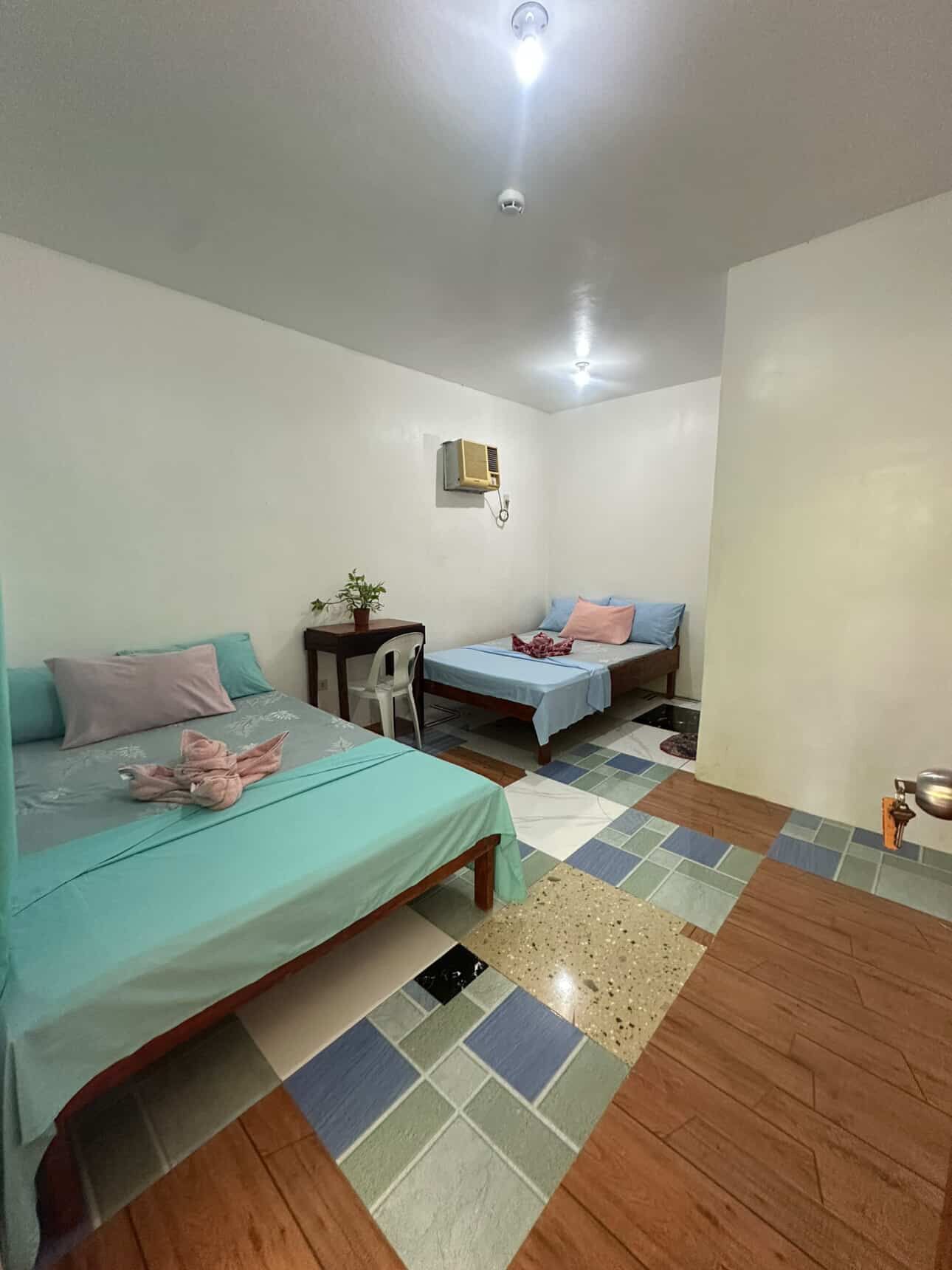 Una habitación pequeña y bien iluminada con dos camas, un escritorio y una silla.