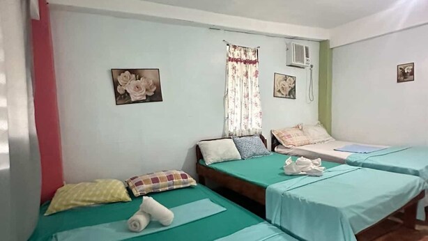 A room with three single beds, each with a green bedspread and white pillows. There are floral wall decorations and a window with a floral curtain. - moonlight inn catangnan  (General Luna)