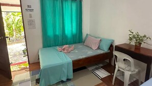 Ein kleiner, gut beleuchteter Raum mit einem Bett, einem Schreibtisch und einem Stuhl. Es gibt ein Fenster mit Vorhängen, eine Tür und ein Schild an der Wand.