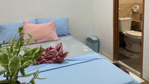 Ein kleiner, sauberer Raum mit einem Bett, einem Nachttisch, einem Mülleimer und einer Topfpflanze.