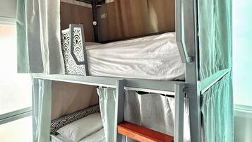A bunk bed with a wooden ladder, a patterned headboard, and a window with curtains.
