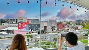 A balcony with a view of a cityscape, including buildings and a road. - Friends Hostel - Phuket Airport (Sa Khu)