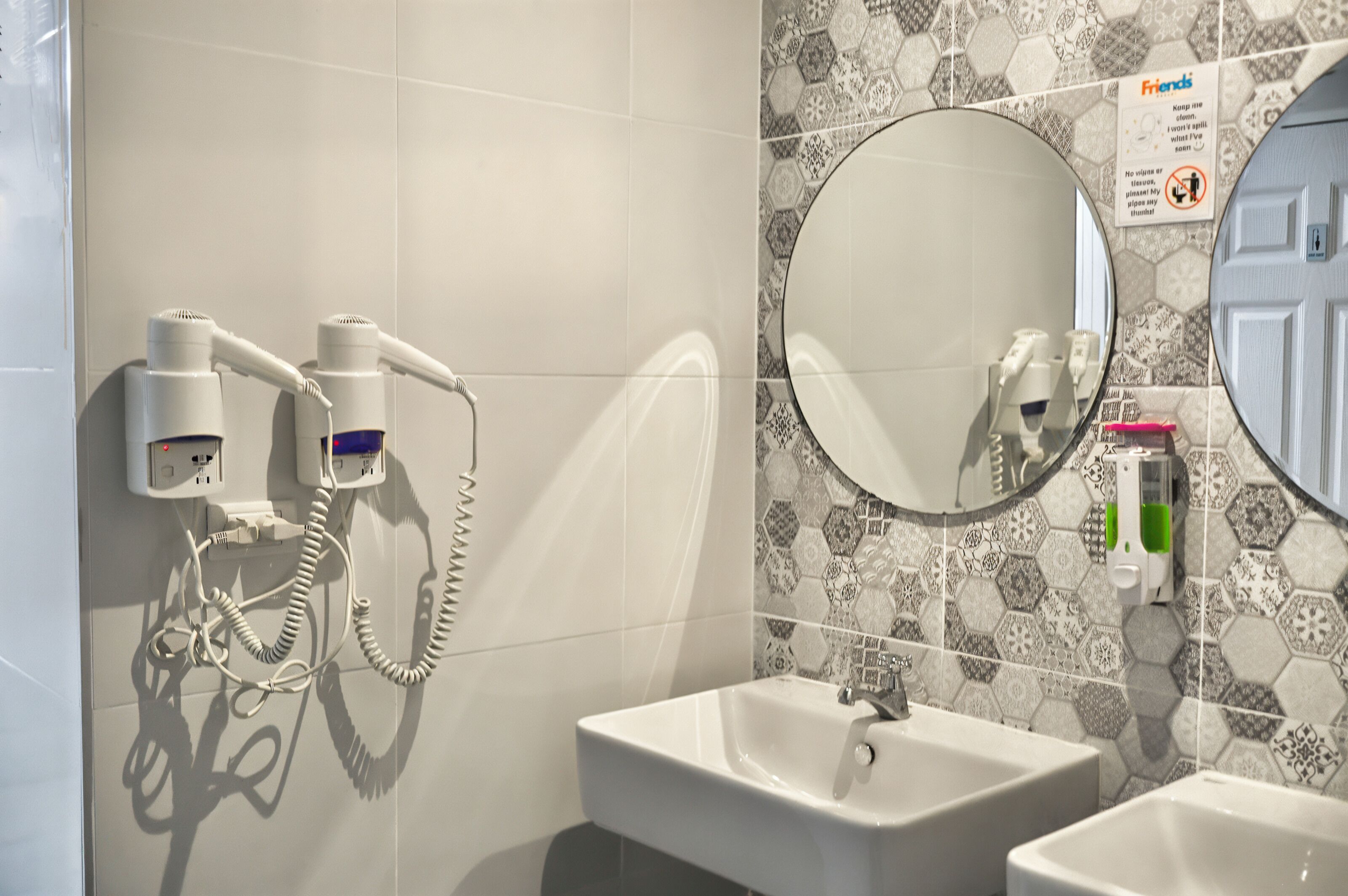 A bathroom with a white sink, a mirror, and a hairdryer mounted on the wall.