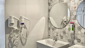 A bathroom with a white sink, a mirror, and a hairdryer mounted on the wall.