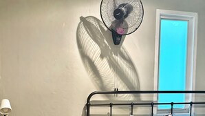 A bedroom with a bed, a chair, a desk, and a wall-mounted fan. - Friends Hostel - Phuket Airport (Sa Khu)