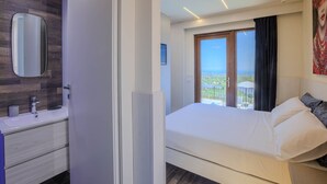 A modern hotel room with a large bed, a bathroom with a mirror and sink, and a balcony with a view. - Beautiful villa with pool, SPA and panoramic sea views, just 10 minutes from the beaches of Pineto (Atri)