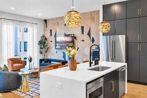 A modern kitchen with a central island, stainless steel appliances, and a large wall-mounted TV.