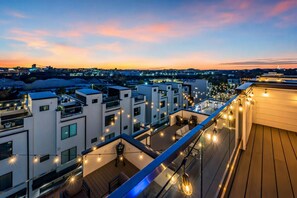 A rooftop terrace with string lights, modern buildings, and a cityscape in the background.