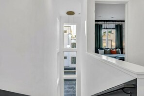 A modern interior with a staircase leading to a bedroom. The room features a large window with curtains, a bed with pillows, and a view of the outside.