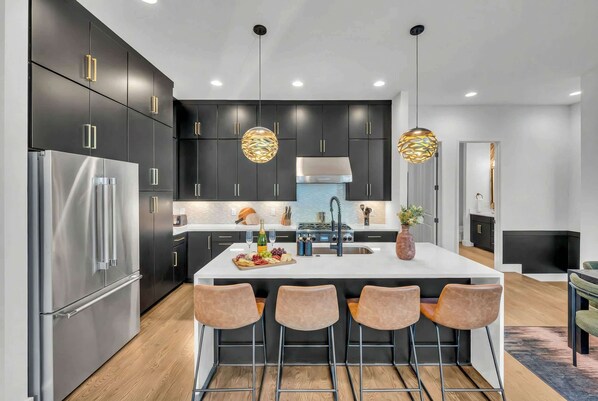 A modern kitchen with dark cabinetry, stainless steel appliances, and a central island with bar stools.