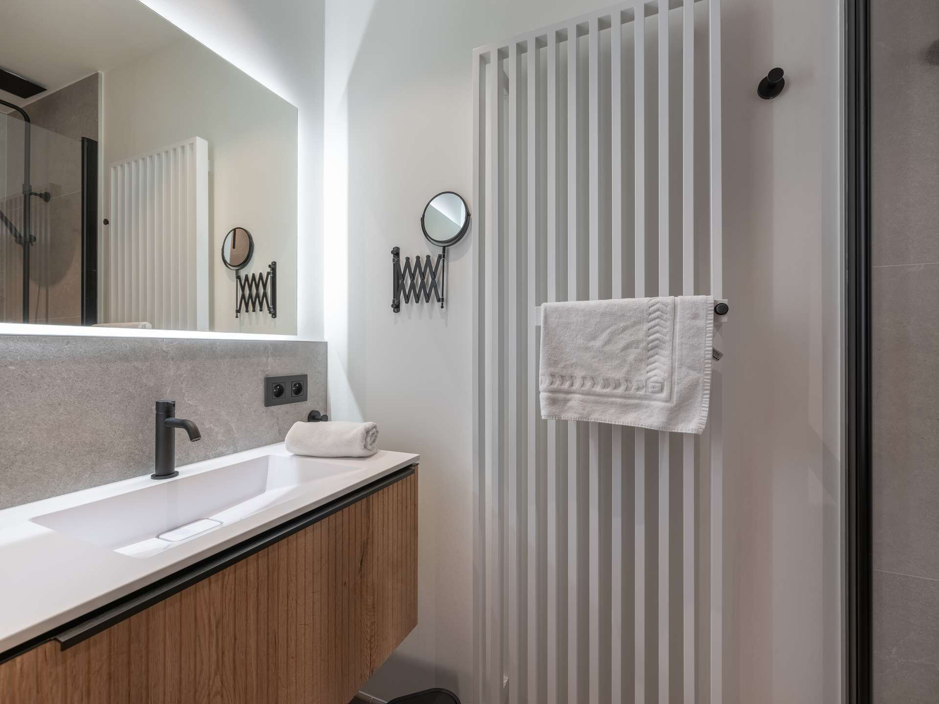 Une salle de bain moderne avec un grand miroir, un lavabo blanc et un porte-serviettes.