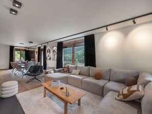 A modern living room with a sectional sofa, a dining table, and a large window with a view of the outdoors. - CHALET ELEGANCE ALPINE LA CHAPELLE D'ABONDANCE (LA CHAPELLE D ABONDANCE)