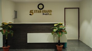 Un espace d’accueil comprenant un comptoir de réception, une horloge et deux plantes en pot.