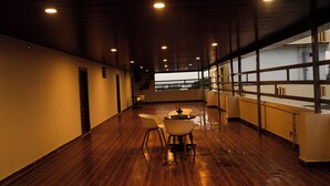 Un vaste couloir doté d’un plancher en bois, un coin salon avec des chaises et une table, et de grandes fenêtres offrant une vue sur l’extérieur.