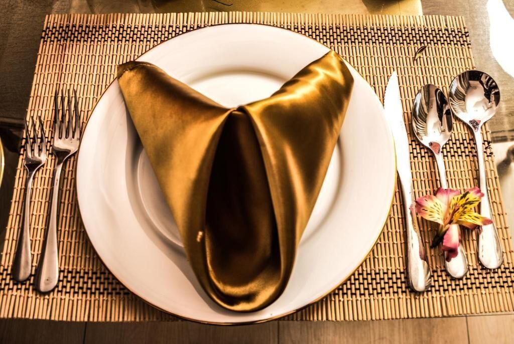A neatly set table with a folded napkin, silverware, and a flower on a placemat.