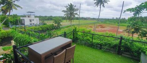 A balcony with wicker furniture overlooking a grassy area with palm trees and a view of a building in the distance.