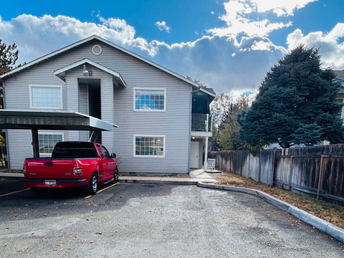 Un bâtiment à deux étages avec un garage, un camionnette rouge garée devant et une clôture en bois.