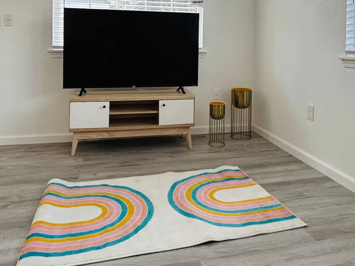 A room with a TV on a wooden stand, a colorful rug, and two gold lamps.