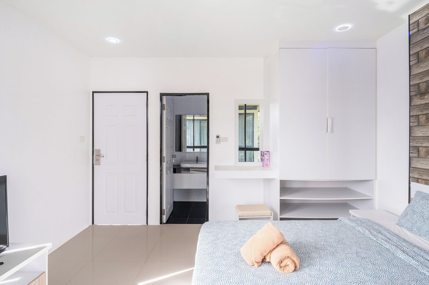 Un dormitorio moderno con una cama, un televisor, un armario y un baño visible a través de una puerta abierta.