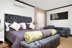 A bedroom with a large bed, a grey sofa, and a painting on the wall. - Craigavon House by Tanaka Kingdom  (Fourways)