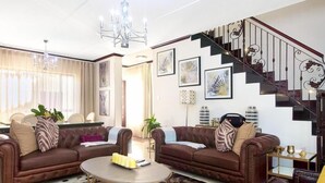 A living room with two brown leather sofas, a coffee table, and a staircase with ornate railings. - Craigavon House by Tanaka Kingdom  (Fourways)
