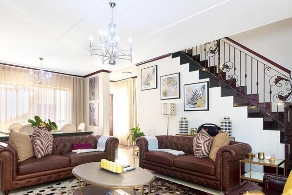 A living room with two brown leather sofas, a coffee table, and a staircase with ornate railings.