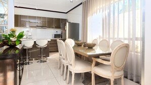 A modern dining area with a glass-top table, white upholstered chairs, and a bar with stools. - Craigavon House by Tanaka Kingdom  (Fourways)