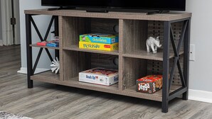 Ein Holz-Fernsehschrank mit drei Ablagen, auf denen Gesellschaftsspiele und eine kleine Elefantfigur stehen.