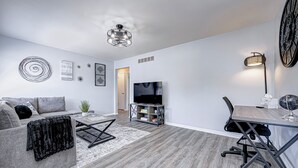 Ein modernes Wohnzimmer mit grauem Sofa, Couchtisch, Fernseher und Essbereich mit Tisch und Stühlen.