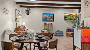A dining area with a round wooden table set for four, surrounded by wooden chairs. There is a sofa with a cushion and a small side table with a lamp and decorative items. The walls are adorned with framed artwork and a quote. - Chic Zen-Inspired Oasis w/ Patio & Red Rock Views (Sedona)