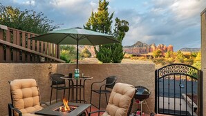 An outdoor patio with two cushioned chairs, a table with a fire feature, and a green umbrella. - Chic Zen-Inspired Oasis w/ Patio & Red Rock Views (Sedona)