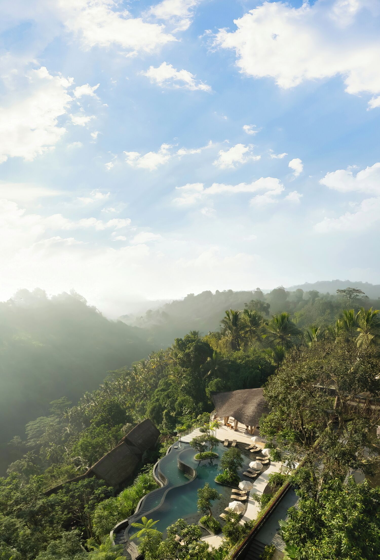 A resort with a pool area surrounded by lush greenery and a view of mist-covered hills.