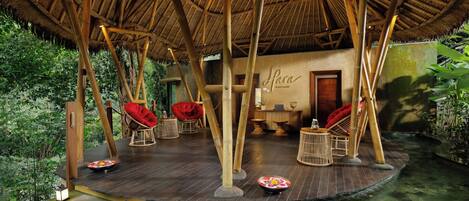 A bamboo-framed outdoor seating area with a thatched roof, a small water feature, and a sign reading "Lana."