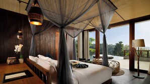A bedroom with a canopy bed, a wooden floor, a bedside table, a nightstand, a lamp, a window with a view of greenery, and a small table with a chair outside.