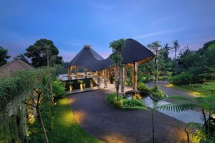 Un resort con construcciones de techo de paja, un elemento acuático central y abundante vegetación.