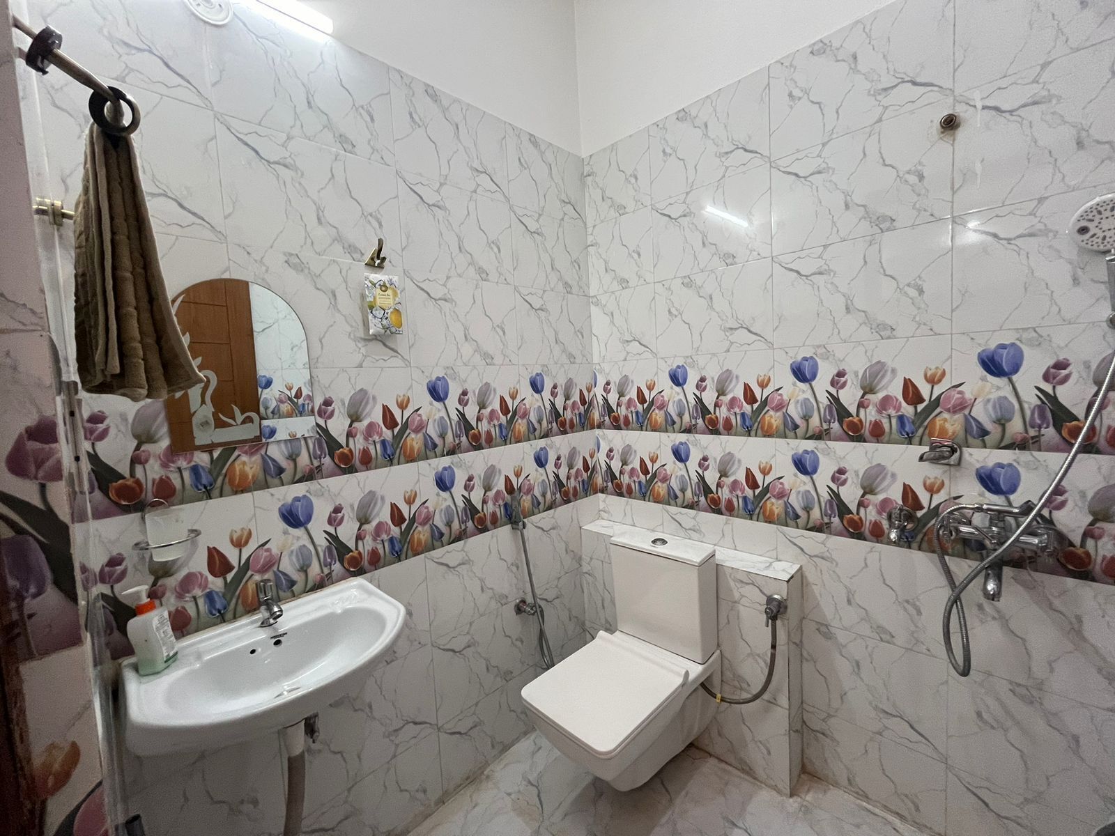 A bathroom with a sink, toilet, and shower. The walls are tiled with a floral pattern.