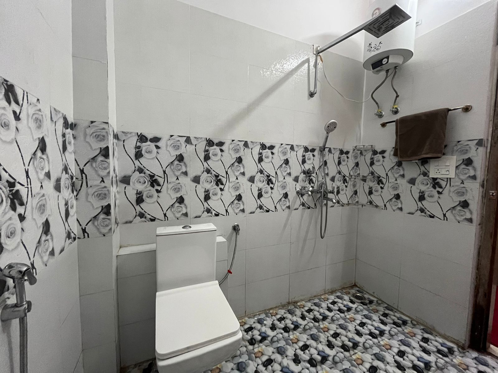 A bathroom with a toilet, shower, and tiled walls with a floral pattern.