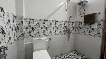 A bathroom with a toilet, shower, and tiled walls with a floral pattern.