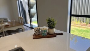 A kitchen counter with two floral-patterned cups and a potted plant on a wooden board. - The Cosy Cottage  (Ararat)